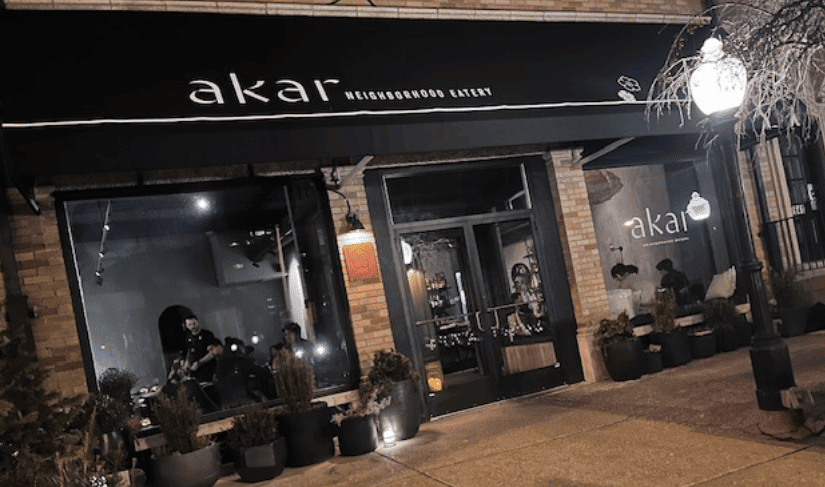 front entrance to the restaurant Akar, logoed awning, double doors, green plants, street lights