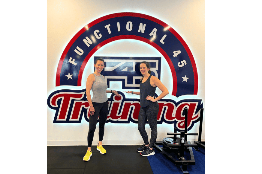 2 women standing against F45 signage, smiling after their funcational fitness workout at F45.