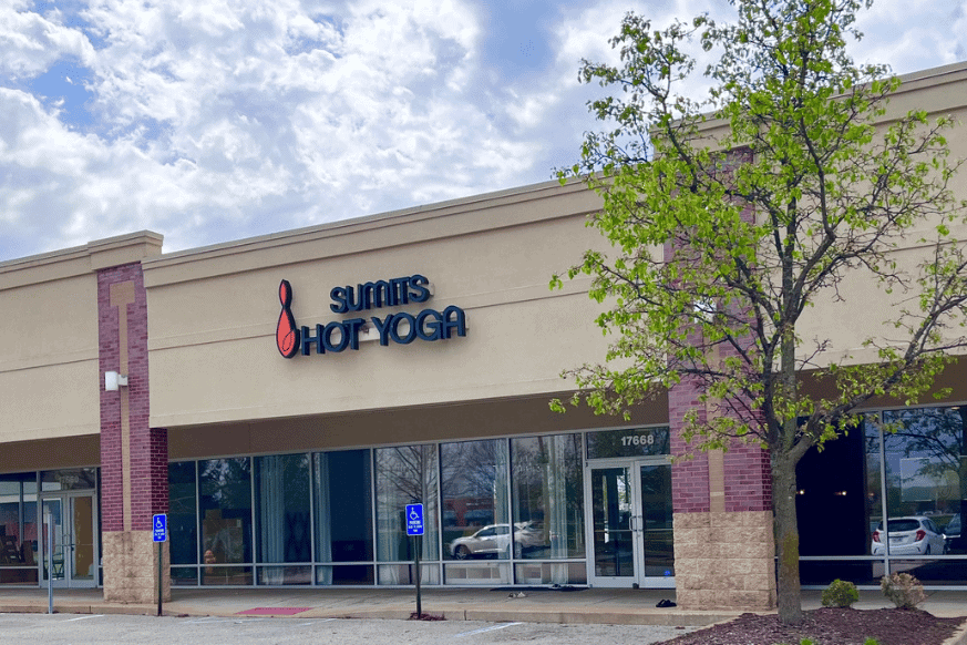 exterior of Sumits Hot Yoga; strip mall location with handicapped parking spaces in front with blooming tree.