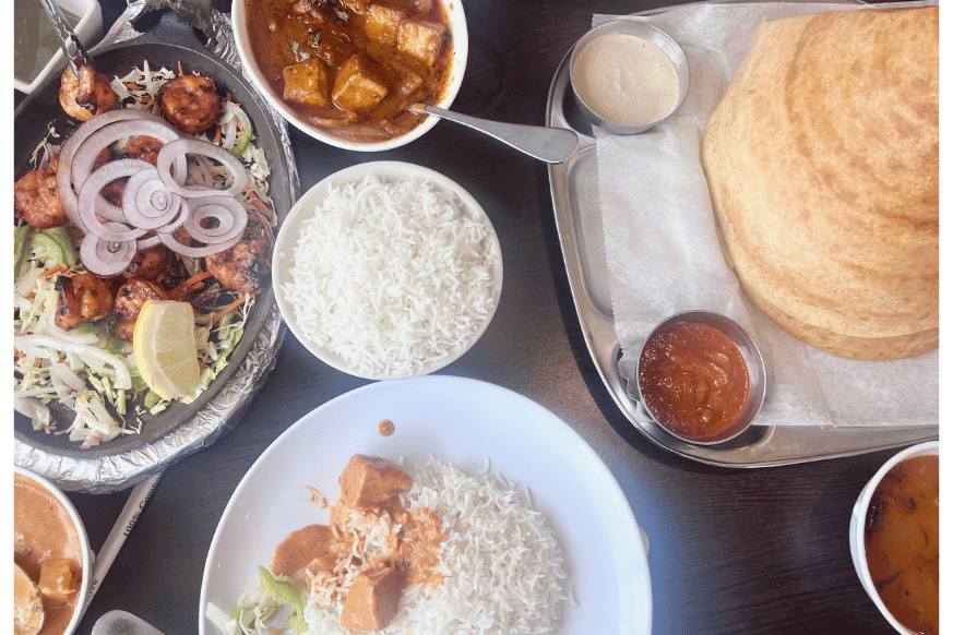 image showcasing several indian foods from view above,  Several plates, bowls and serving dishes on a table with bright colored sauces. 
