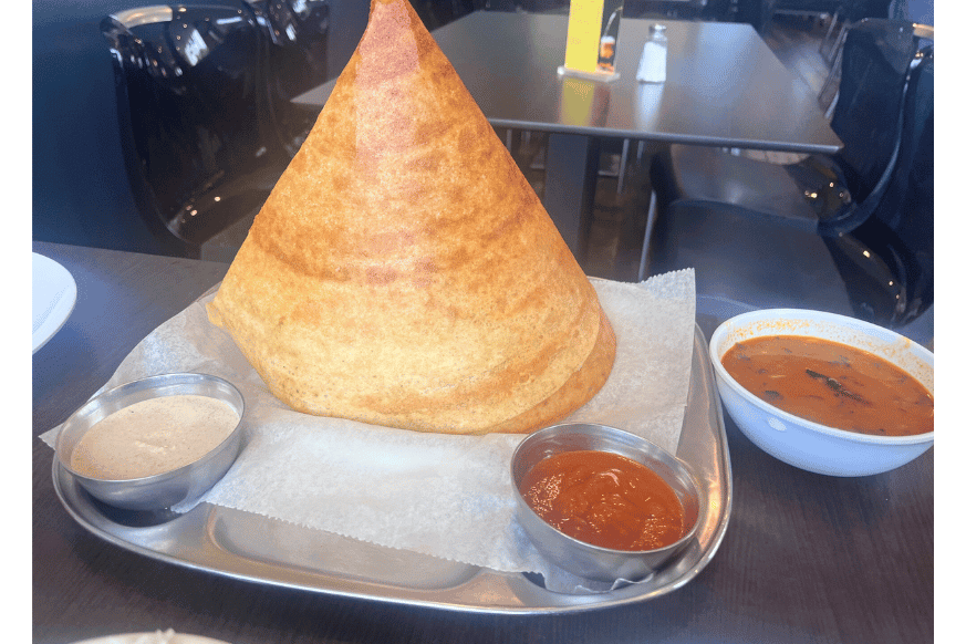 cone dosa, thin crispy crepe plated in a a cone or pyramid shape and served on a silver platter with 2 dipping sauces.  The mild peanut sauce is beige and the spicy tomato is red