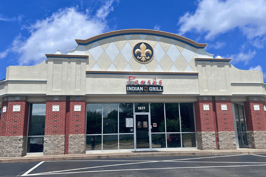 exterior of Persis Grill.  brick and concrete building in a strip mall with fleur de lei emblem and logo.  glass windows.   