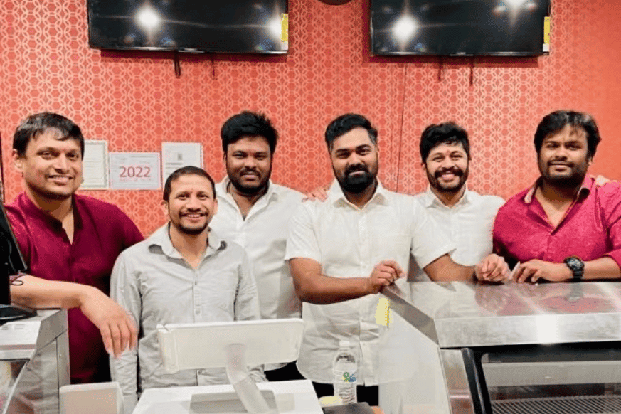 6 indian men and owners of Persis Indian grill are shown smiling in front of the cash register at their restaurant in the suburbs of St. Louis, MO. 