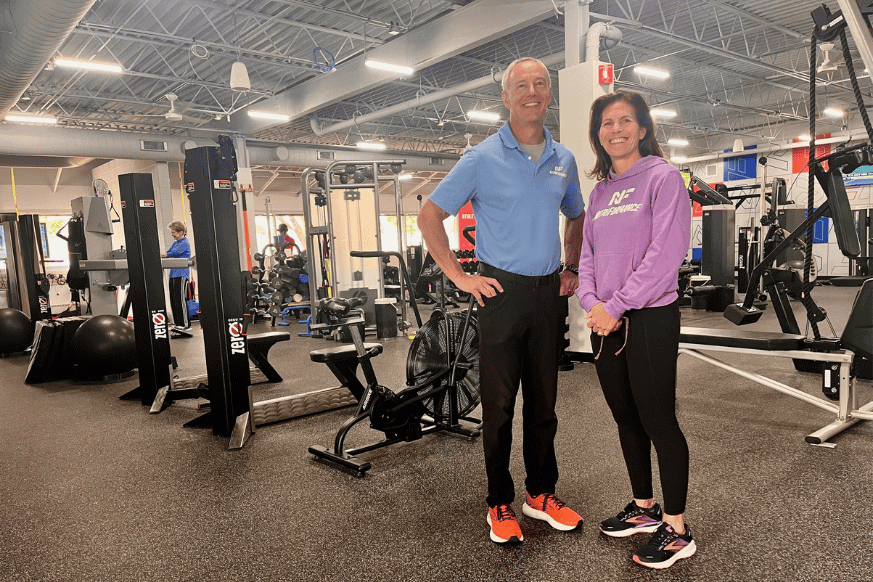 NutriFormance St. Louis owners, husband and wife duo, smile in front of the strength training equipment on the gym floor.  