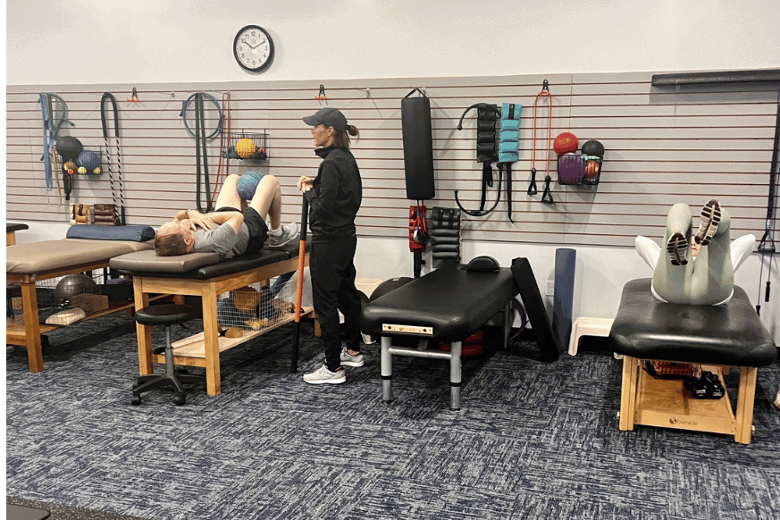 Personal trainer working one-on-one with a client at NutriFormance.  Client is shown doing sit-ups with a ball between his legs while personal trainer watches.  