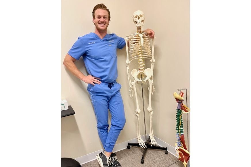 Dr Drew Rapert, chiropractor, smiling next to his life size skeleton model in his chiropractic office