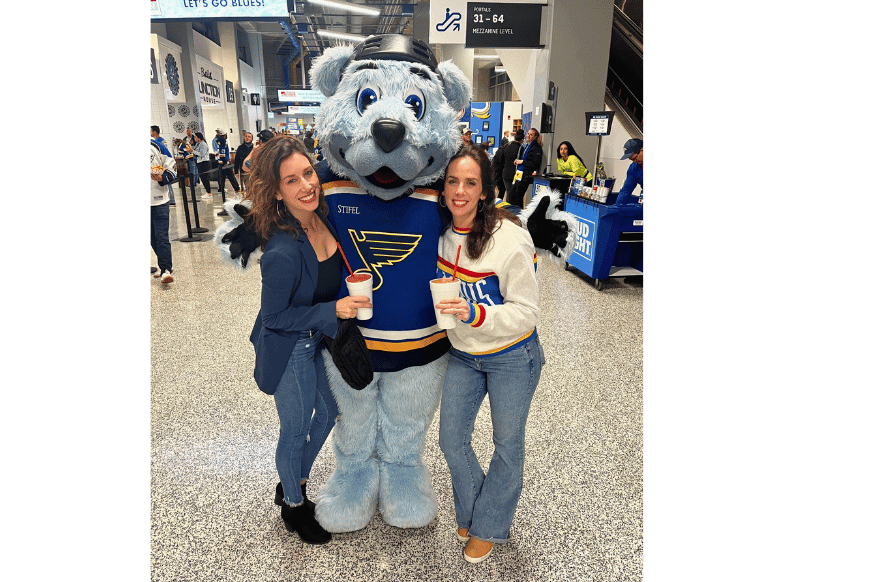 two women pose with blue bear mascot of the st louis blues in the halls of enterprise center