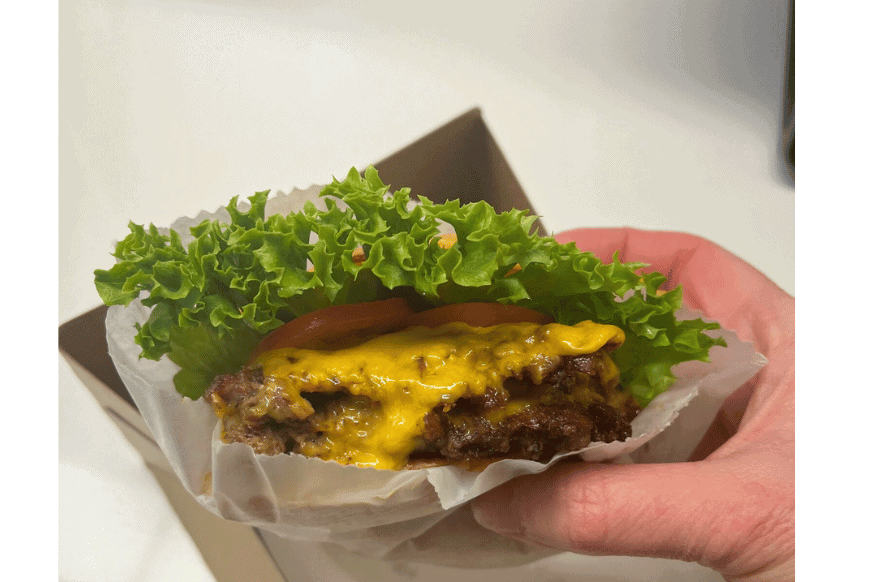 zoom in of the Shake Shake double shack burger oozing with cheese and a large piece of lettuce and tomato tucked in.