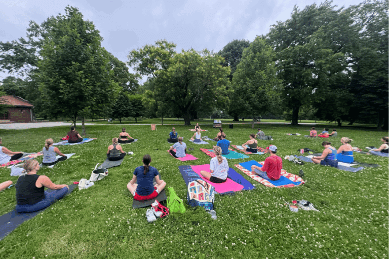 several yoga participants seated on colorful yoga mats in the park