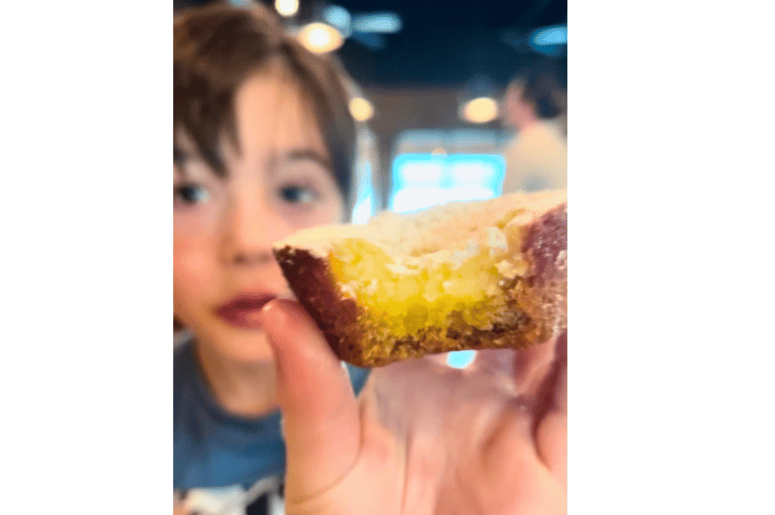 young boy holding up an already bitten gooey butter cupcake from mac's local eats.  the inside showcases the crispy brown bottom and edges with a light yellow, gooey center.  