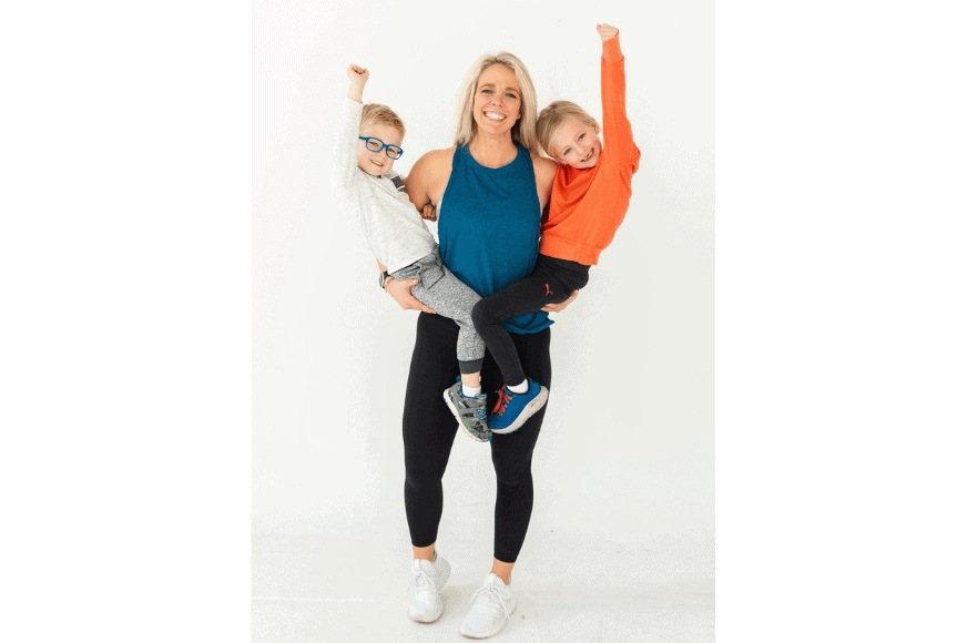  muscular blonde woman (Katy Ferguson) in workout gear holds her two children proudly a little boy on the left and a little girl on her right.   