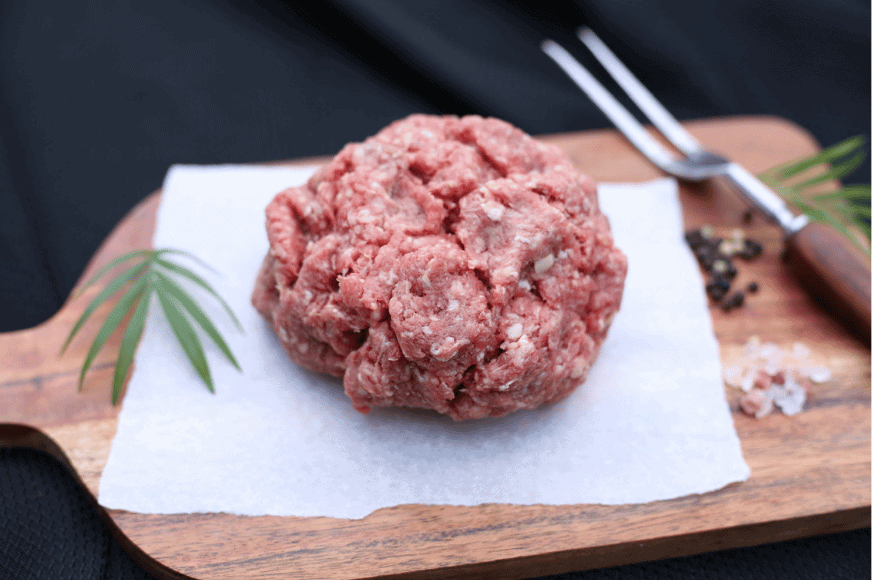 a ball of ground meat zoomed in to show texture and fat. placed on top of a wood cutting boar with a meat fork and large crystals of salt & pepper. get this grass-fed meat delivered from The Log cabin Ranch