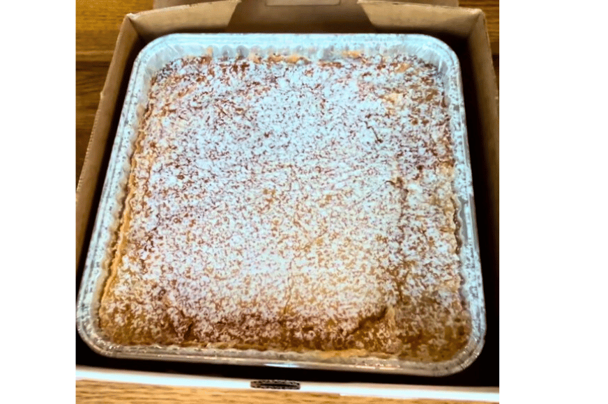 A square aluminum tin filled with gooey butter cake from Gooey Louie in St Louis.  Yellow cake thats more brown on the edges topped with white powdered sugar.