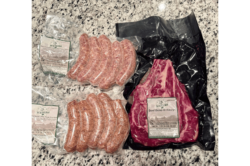 2 packages of grass-fed brats and one beef bone-in ribeye still wrapped in plastic after delivery from The Log Cabin Ranch