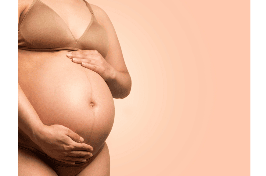 zoom in of a very pregnant women belly.  she has one hand on top of her belly and one on the bottom.  she is wearing a nude bra.