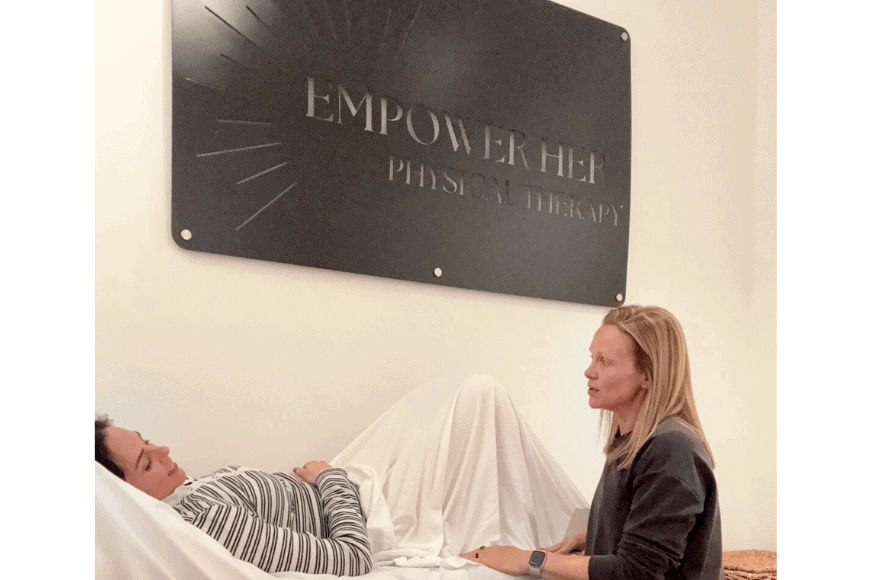 a women with dark hair and a black and white striped shirt on is lying on an exam table with a white sheet across her waist and legs.  the pelvic floor physical therapist is a middle aged women with long blonde hair  is seated next to the exam table talking to the patient