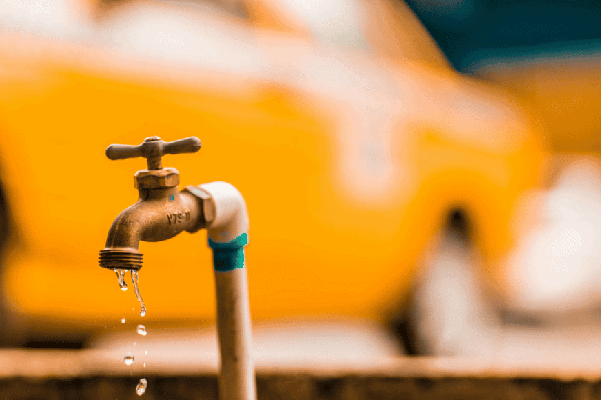 a singular faucet shows water leaking out.  yellow faded car driving by in the background