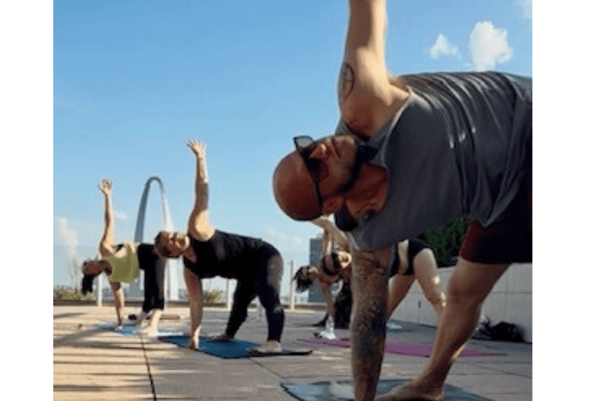 triangle pose yoga on the rooftop with views of the st louis arch, big blue sky