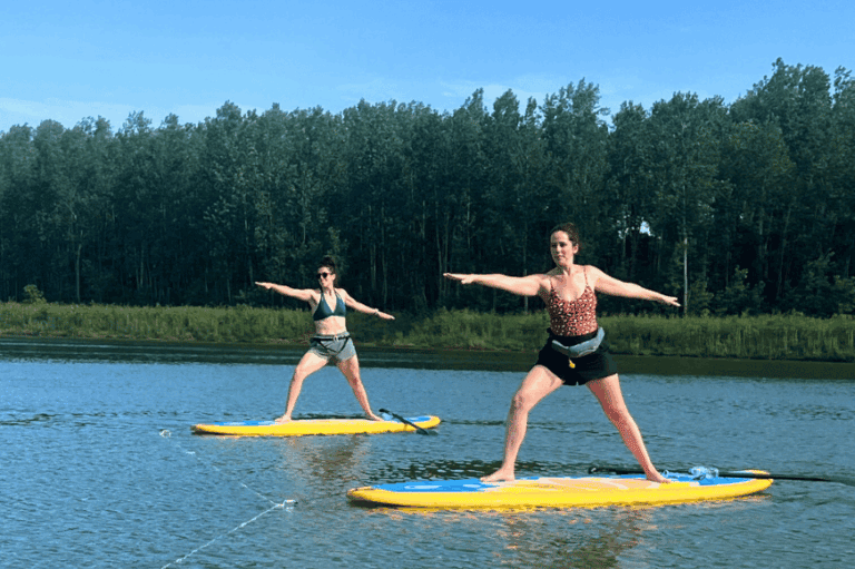two women doing warrior yoga pose on a paddleboard in the middle of a lake