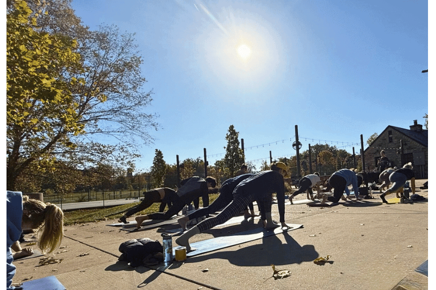 women holding a plank position in a group barre class in francis park.  bright sun and fall trees