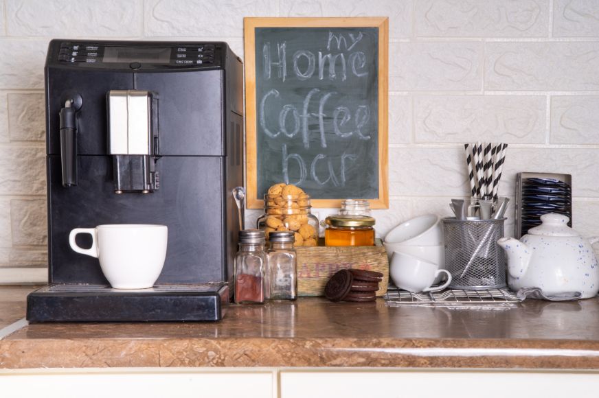 at home coffee station including coffee maker, tea pot, mugs, straws and other jars and shakers of additives like cinnamon and honey.