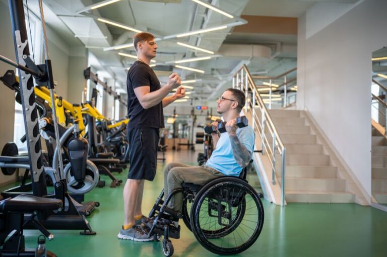 man in wheelchair lifting weights with guidance from his personal trainer at the gym