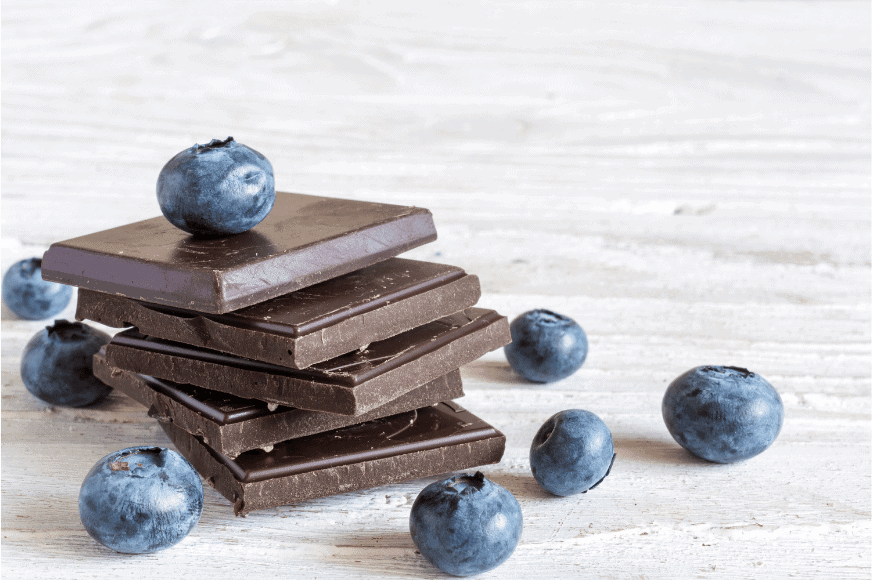 a stack of 5 dark chocolate squares with blueberries on top and nearby