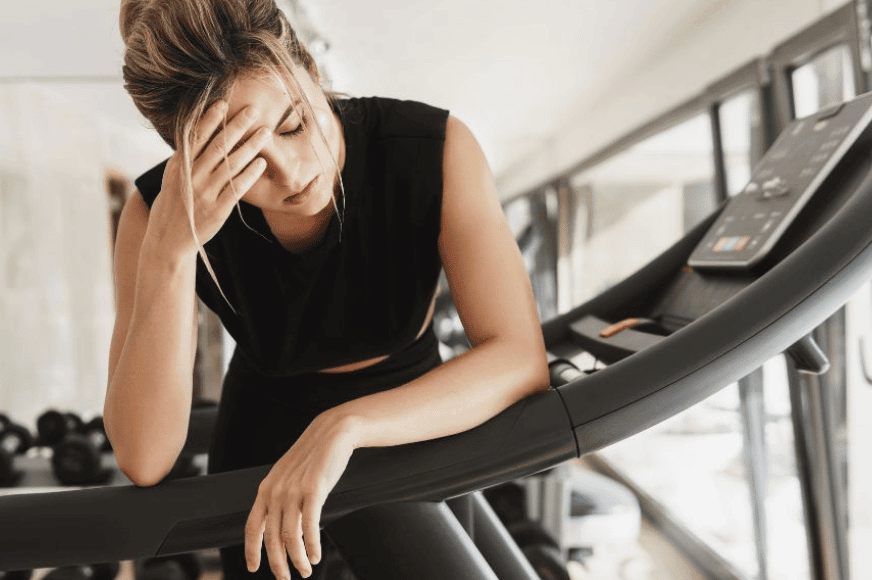 women on a treadmill stopped and putting hand on head looking exhausted.  if you feel fatigued after working out, it could be a sign you need more iron