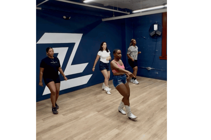 ladies of all races and ages smiling & learning to urban line dance from Lauriel Bristol of Her Wellness by Her