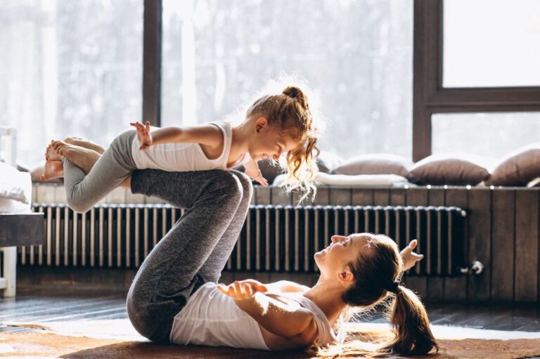 mom on the floor on her living room playing "airplane" a yoga post that holds her daughter on her shines high in the air.