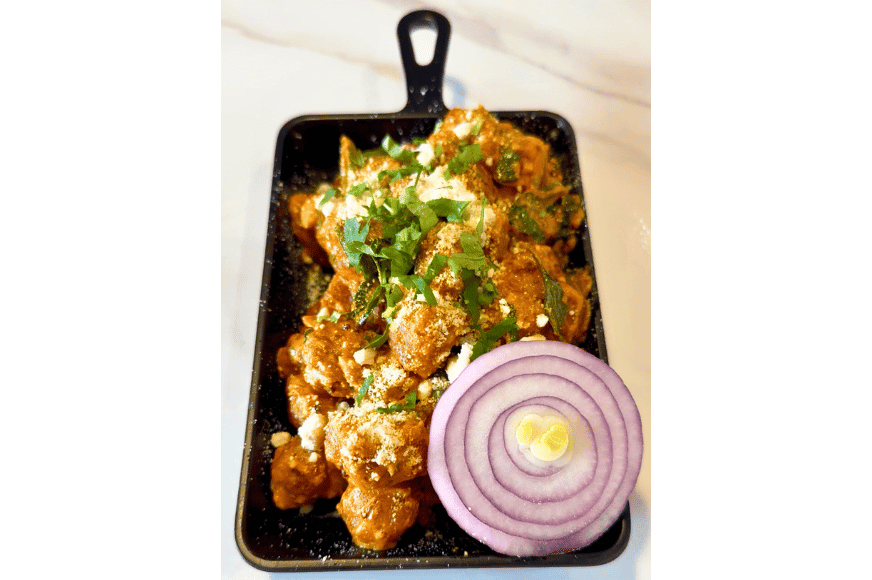 a black skillet with 555 baby corn appetizer, orange deep fried chunks topped with green herbs and a white cheese
