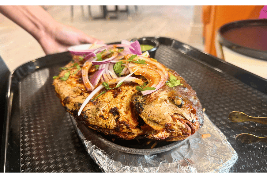 a look at the whole fish dish, kakinada tandoori chepa, with mouth eyes and all served on a silver platter and topped herbs, chili and with slices of red onion