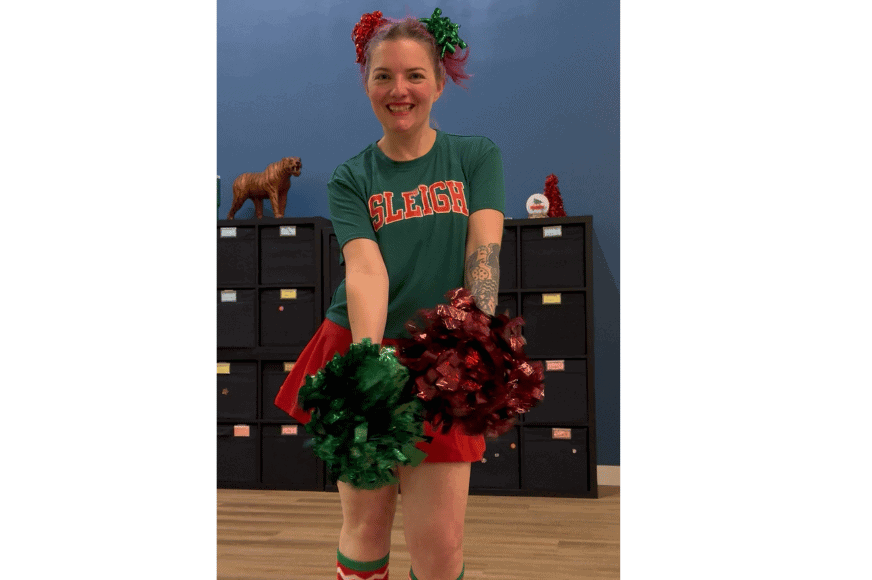 cindy henry, lead instructor of pom squad fitness showing smiling and shaking her pom poms while dressed in a red & green cheerleading outit