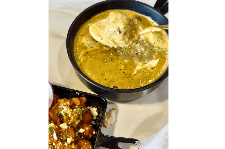 a gold spoon holds a kafta ball and yellow sauce over a bowl of mughali malai kofta at persis indian grill in ballwin