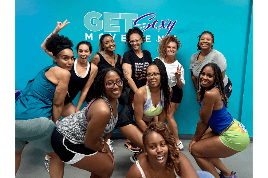 a group of smiling women in front of a blue wall with the "Get sexy movement" logo on it wearing athletic clothes after twerkercise group fitness class in st louis