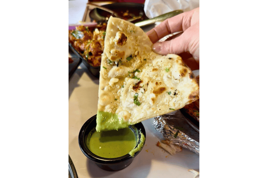 a triangular piece of garlic naan that was just dipped in a green sauce is held up for the camera