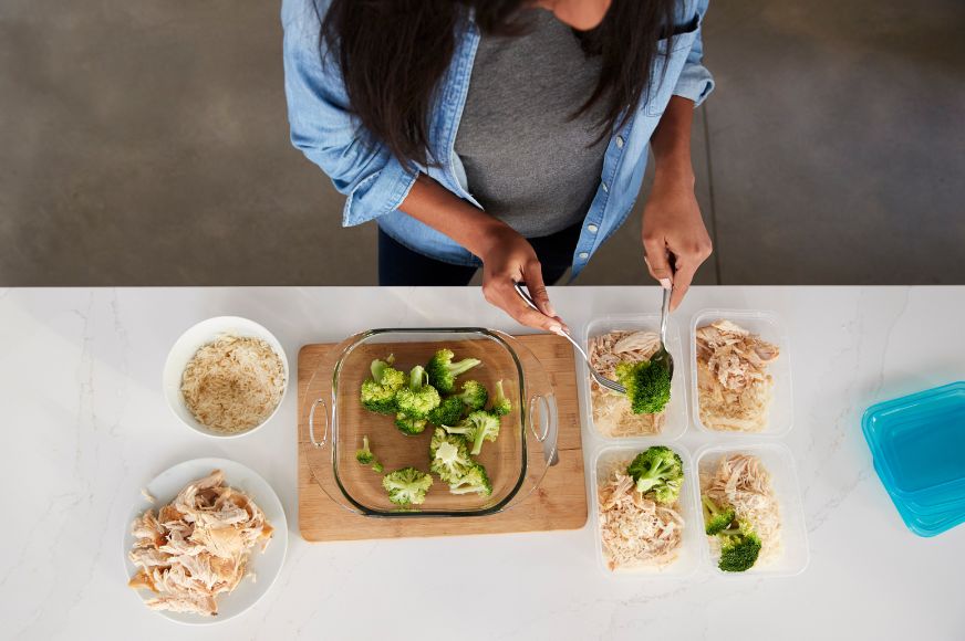 woman shown prepping small containers with brown rice, shredded chicken breast and broccoli. meal prep image