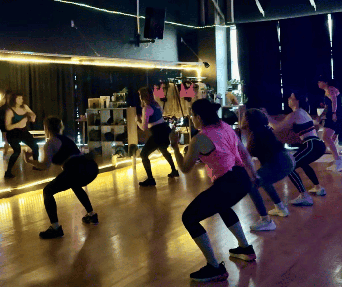 even though its morning, bloom dims the lights and turns the music up during cardio dance. many women shown doing a squat at cardio dance at bloom fitness studio featured in 3 group fitness classes to know