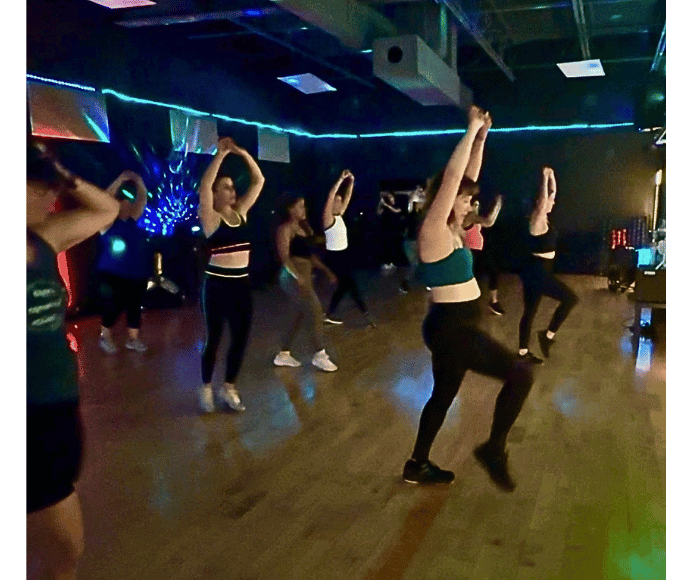 multiple women wearing athletic wear during a dance fitness class have their arms in the ear and one knee lifted