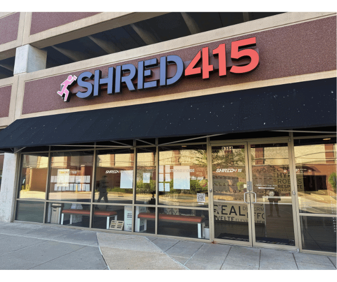 the exterior of shred415 shows all glass windows and black awning and large black, grey and orange logo