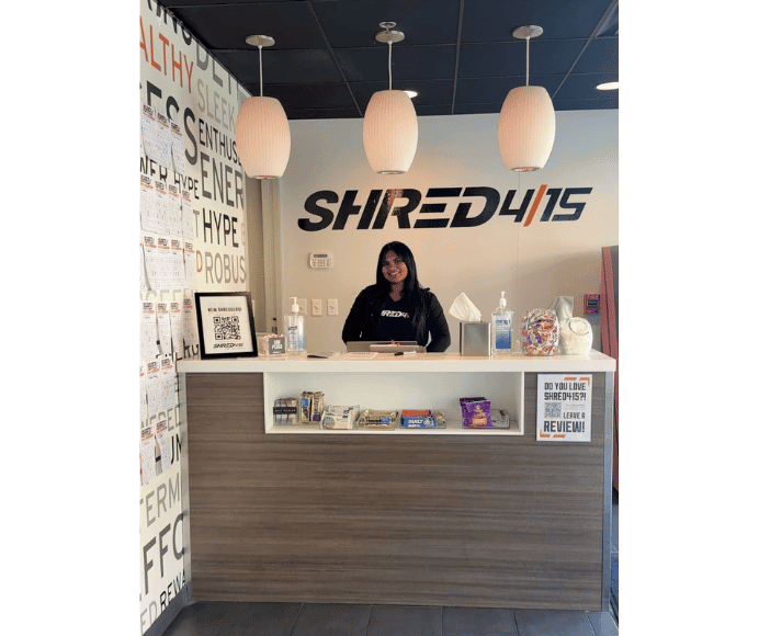 lobby of shred415 where 3 lights hand over a desk with the shred logo in the background and smiling women is waiting behind the desk to assist