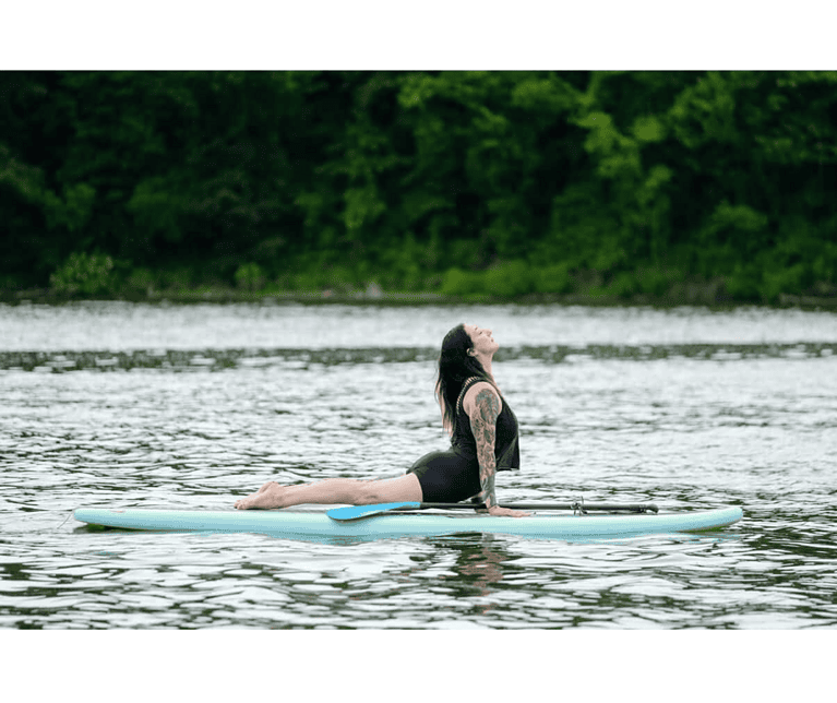 women shown in cobra yoga pose on a paddleboard in the middle of a still lake. mandi gray sup