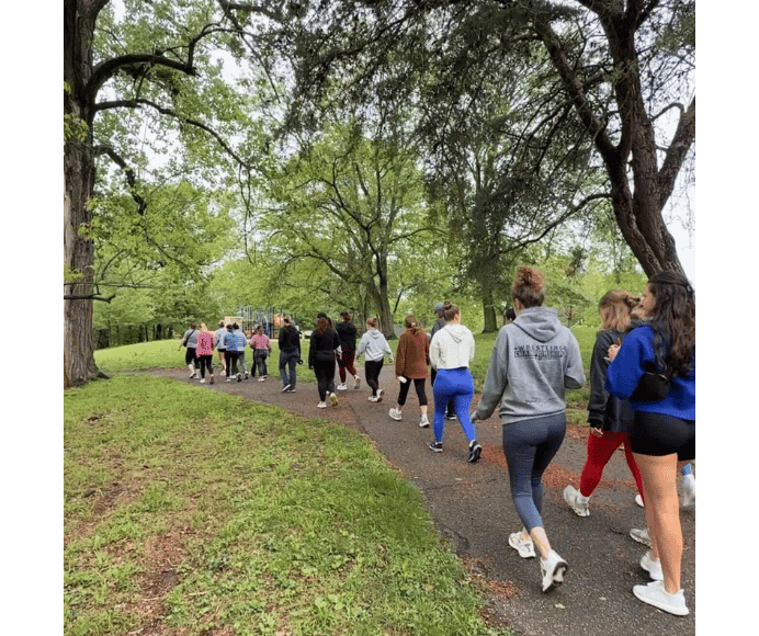 large group of women walking in a park setting with tall trees and green grass