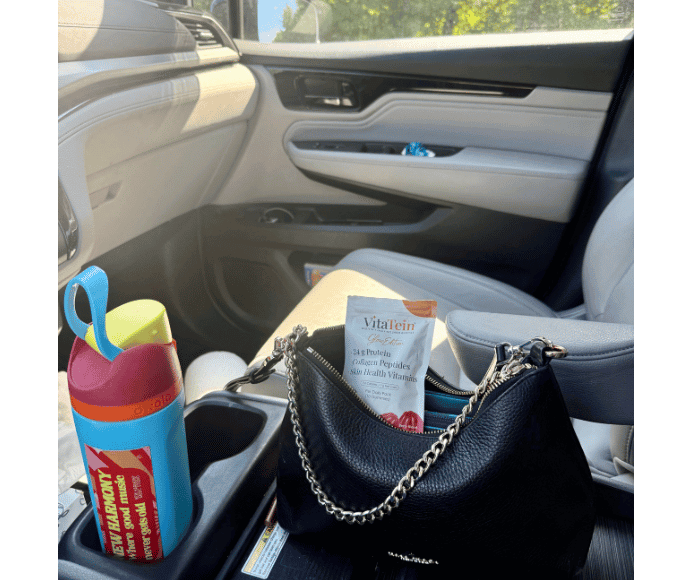 the inside of a womans car showing her black her with vitatein protein gummies and her waterbottle